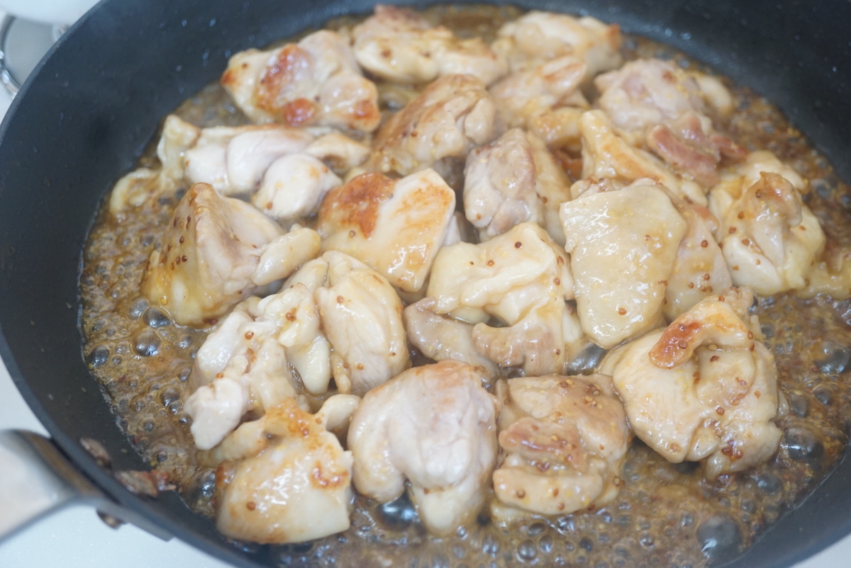 Bite size piece chiken thighs being shimmered with sauce in pan