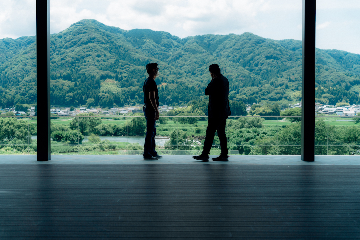 Two men standing by the window overlooking the forest