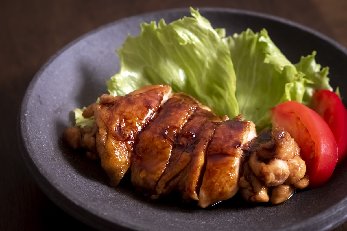 Chicken teriyaki with teriyaki color, with lettuce and slices of tomato on a black plate
