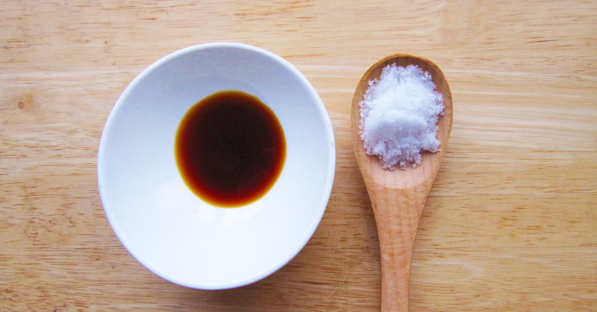Soy sauce in a white bowl and salt on a wooden spoon