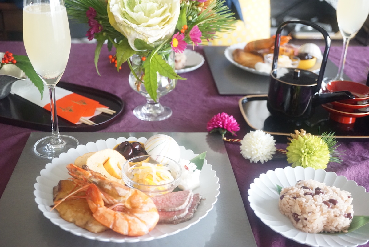 Osechi (shrimp, datemaki, namasu, kuromame and duck meet) and sekihan on a table with glasses of otoso