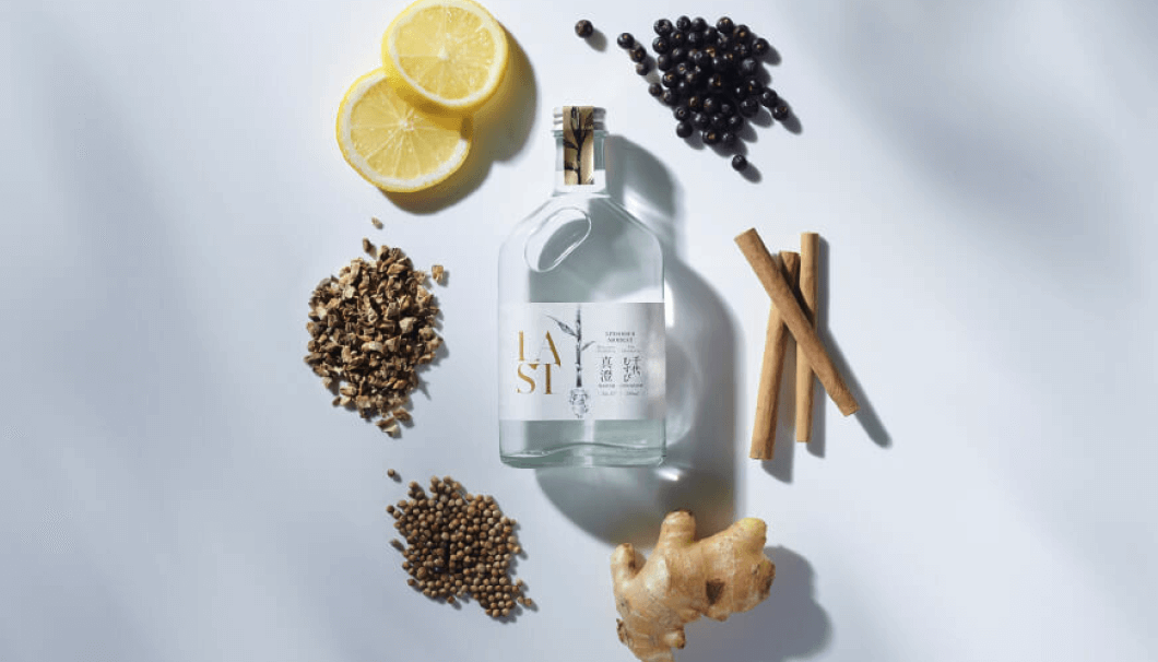 A bottle of LAST, ethical spirit, surrounded by slices of lemon, blueberries, cinnamon sticks, ginger root and peppers