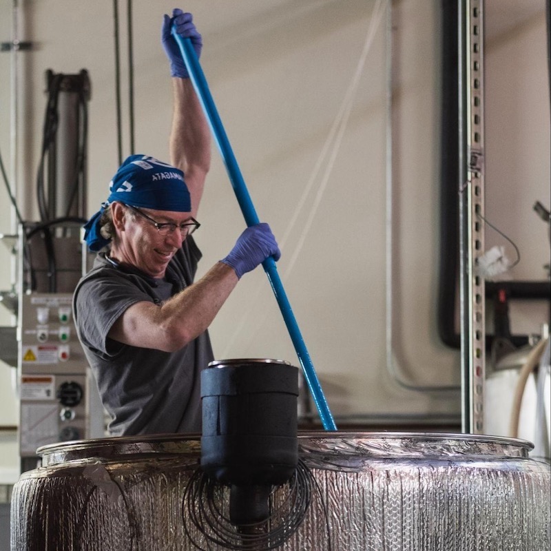 Jake Myrick mixing something in a large barrel with a blue long stick